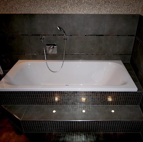 Nach der Sanierung: Moderne Badewanne mit kleinen Fliesen eingefasst und integrierten Strahlern